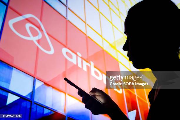 In this photo illustration, a woman's silhouette holds a smartphone with the Airbnb logo in the background.