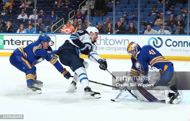 Pierre-Luc Dubois of the Winnipeg Jets is defended by Craig Anderson and Henri Jokiharju of the Buffalo Sabres during an NHL game on March 30, 2022...