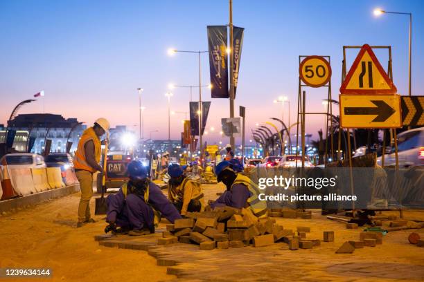 March 2022, Qatar, Doha: Workers pave a path between lanes on the Corniche promenade shortly after sunset in the light of lanterns. Doha will host...