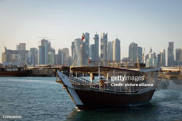 March 2022, Qatar, Doha: A dhow boat with tourists returns from a tour in front of the skyline of West Bay Doha to the jetty on the Corniche...