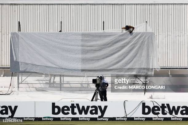 Worker covers the digital sign board with a cover as play has been delayed due to a technical malfunction of the sign board ahead of the first day of...
