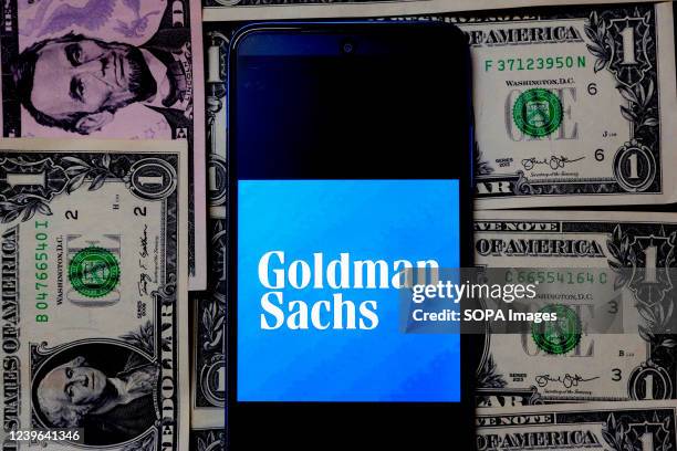 In this photo illustration, a Goldman Sachs logo seen displayed on a Smartphone with a background of American dollar currency notes.