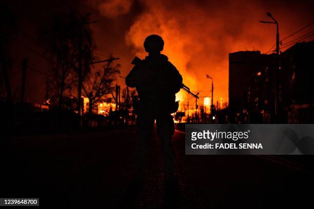 Member of the Ukrainian special forces is seen in silhouette as he stands while a gas station burns after Russian attacks in the city of Kharkiv on...