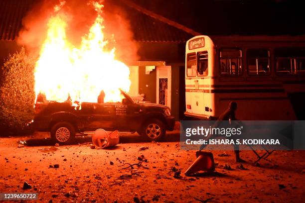 Protester throws an object at a bus next to a burning police car during a demonstration outside the Sri Lankan president's home to call for his...