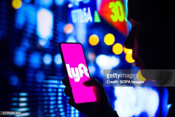 In this photo illustration, a woman's silhouette holds a smartphone with the Lyft logo displayed on the screen.