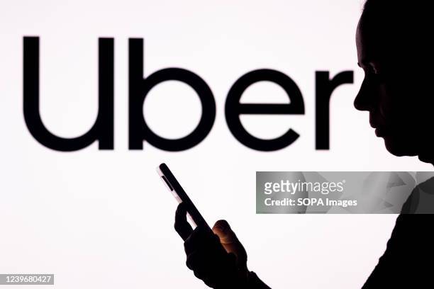 In this photo illustration, a woman's silhouette holds a smartphone with the Uber Technologies logo in the background.