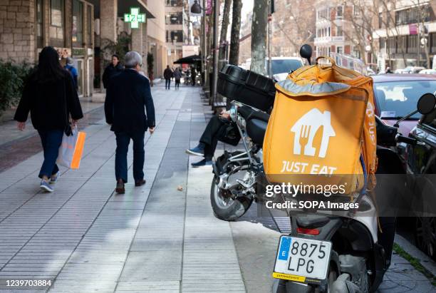 Pedesrians walk past a motorbike courier from the online food order and delivery service company, Just Eat, in Spain.