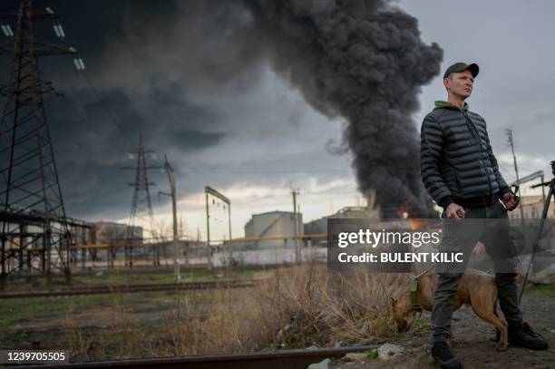 Man stands with his dog as smoke rises after an attack by Russian army in Odessa, on April 3, 2022. - Air strikes rocked Ukraine's strategic Black...