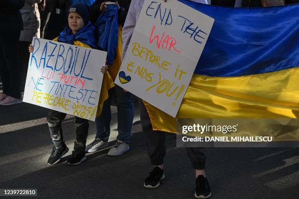 Child wearing the Ukrainian flag holds a placard reading in Romanian "Putin's war is targeting each and every one of us!" during a protest against...