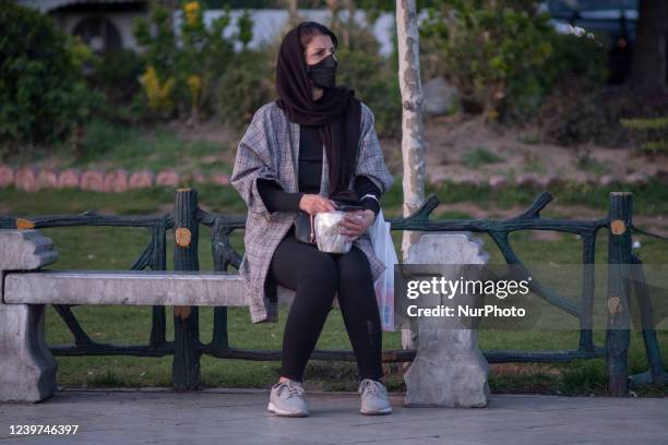 An Iranian woman wearing a protective face mask holds a food container as she sits on a street-side near a holy shrine in northern Tehran on the...