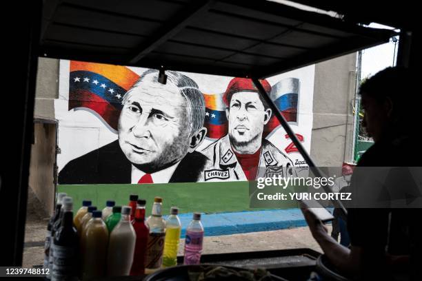 Young man uses a cell phone as he waits for costumers inside his soft drinks stall in front of a mural painted by the Zapatista mural brigade from...