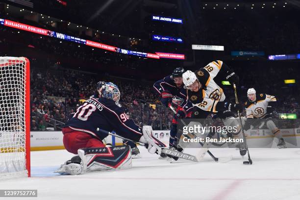 David Pastrnak of the Boston Bruins attempts a shot on goal against Sean Kuraly and Elvis Merzlikins of the Columbus Blue Jackets during the second...
