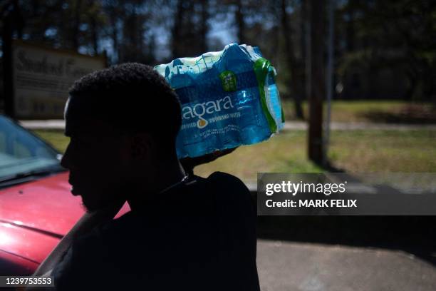 Man carries a case of water given out by Operation Good at an apartment complex in Jackson, Mississippi on March 24, 2022. - Every morning, 180...