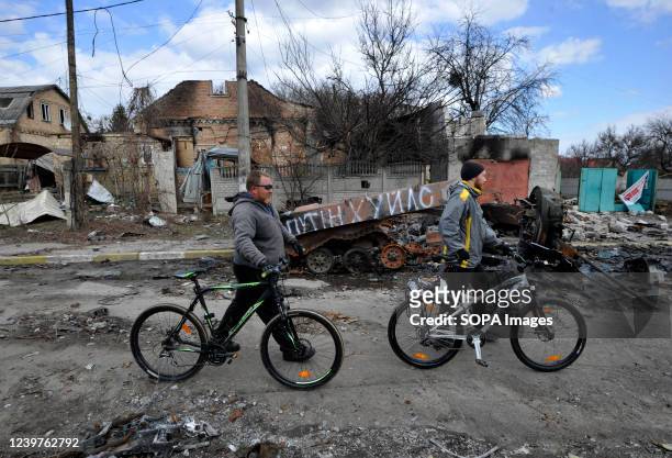 Men push their bikes past wrecked Russian military equipment in the city of Bucha. After invading Ukraine on February 24th, Russian troops took up...