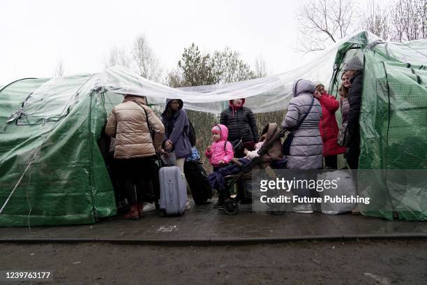 Ukrainians forced to leave Ukraine because of the Russian invasion hide from the rain under the tents as they stand in line at the Ukrainian-Polish...