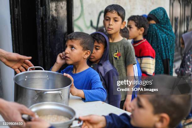 Palestinian children seen in a line with pots and pans to get soup from a center of a local charity group that offers free food during the holy month...