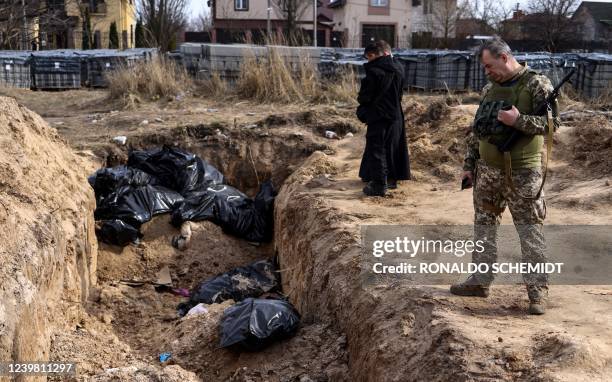 Ukranian soldier looks at body bags as priests pray at a mass grave in the grounds surrounding the St Andrew church in Bucha, on April 7 amid...