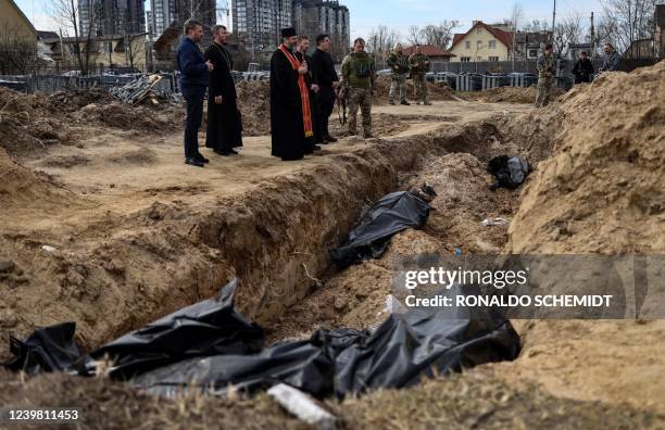 Priests pray at body bags in a mass grave in the grounds surrounding the St Andrew church in Bucha, on April 7 amid Russia's military invasion...