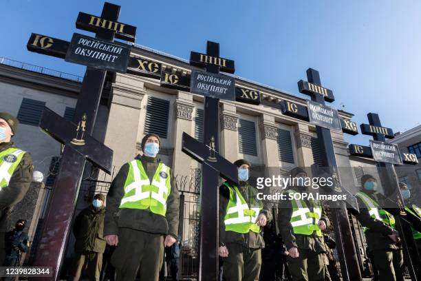 Police officers stand guard behind the grave crosses with an inscription of "Russian Occupation" in front of the Embassy of the Russian Federation in...