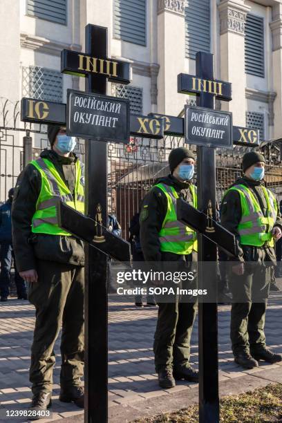 Police officers stand guard behind the grave crosses with an inscription of "Russian Occupation" in front of the Embassy of the Russian Federation in...