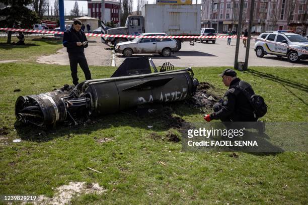 Ukrainian police inspect the remains of a large rocket with the words "for our children" in Russian next to the main building of a train station in...