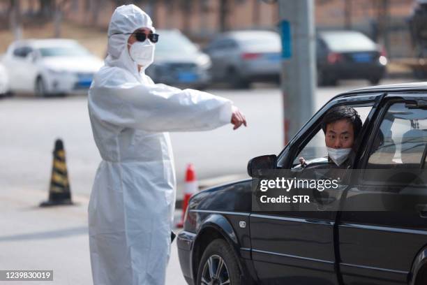 Police officer wearing personal protective equipment speaks with a driver at a checkpoint between two districts as authorities restrict the movement...