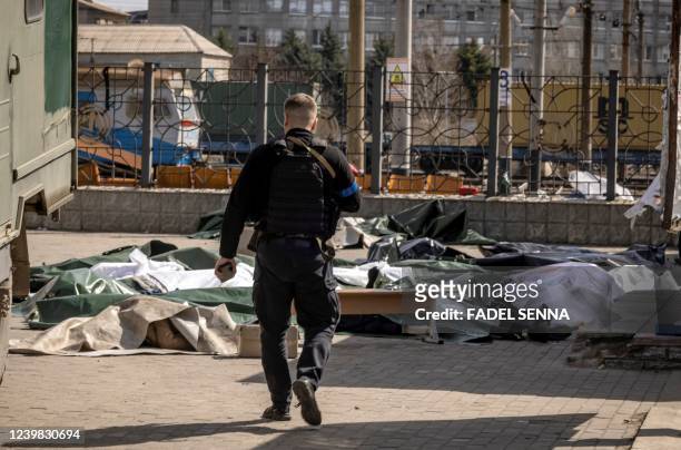 Graphic content / TOPSHOT - A Ukrainian police walks towards bodies covered wiht plastic sheets after a rocket attack killed at least 35 people on...