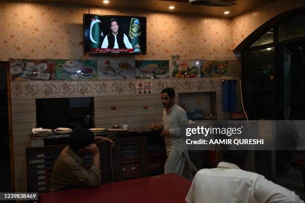 People listen to Pakistan's Prime Minister Imran Khan addressing the nation on television at a restaurant in Islamabad on April 8, 2022. - Pakistan...