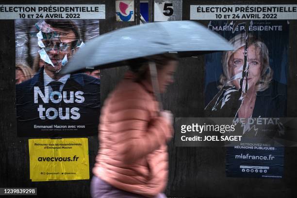 This photograph taken on April 8, 2022 in Paris shows a pedestrian walking past campaign poster of French President and liberal party La Republique...