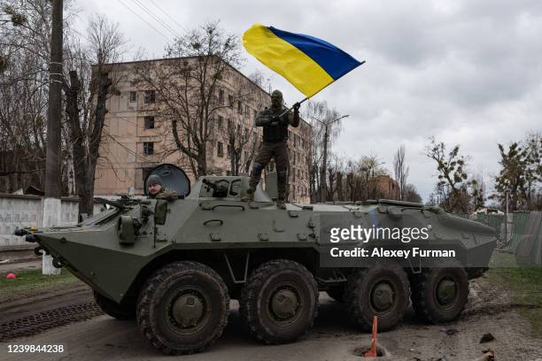 Ukrainian soldier waves Ukrainian national flag while standing on top of an armoured personnel carrier on April 8, 2022 in Hostomel, Ukraine. After...