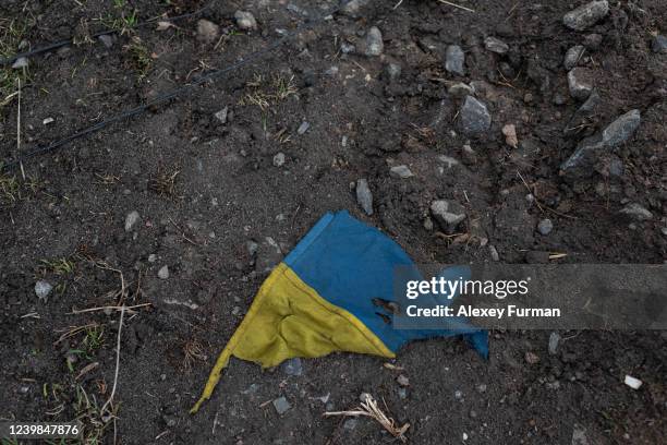 Damaged Ukrainian national flag lies on the ground on April 8, 2022 in Andriivka, Ukraine. The writing says, People, Kids live here. The Russian...