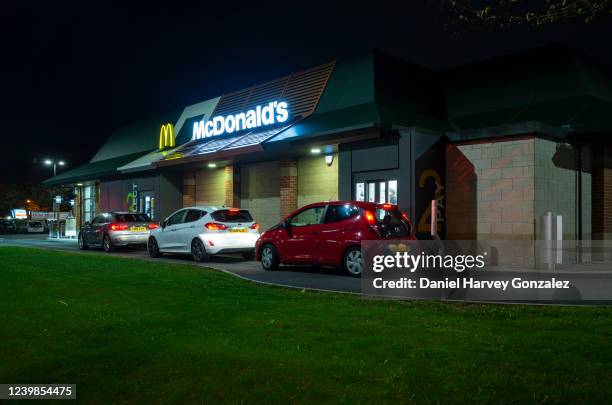 At night time, a series of cars lit by artificial light are served at various points of a drive through operated by fast food giant McDonald's on 6th...