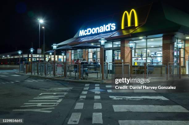 At night time, members of the British public sit inside and outside a branch of fast food giant McDonald's, with the brand's famous golden arches...