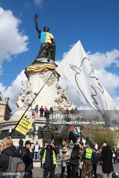 Person holds a banner of a dove of peace in Place de la Republique, in the background, the statue of Marianne, wearing the colours of Ukraine, on...