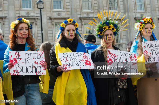 Women wearing floral crowns and holding placards covered in fake blood demonstrate outside Downing Street against war atrocities targeting civilians...