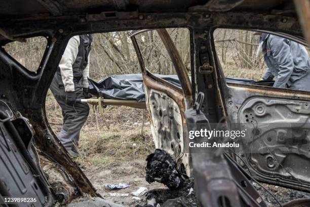 Funeral workers collect the body of a man near to the body of a woman, which is seen huddled-up behind the driverâs seat, both were shot and sat...