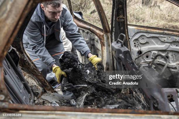 Funeral worker collects the body of a woman, which is seen huddled-up behind the driverâs seat of a car, both were shot and sat ablaze accordingly...