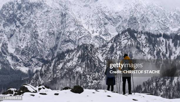 Hikers looks out over the snow covered mountains near the Ritzau alp in the Kaiser Mountains, Austria, during changeable weather with a mix of rain,...