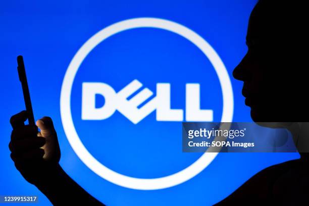 In this photo illustration, a woman's silhouette holds a smartphone with the Dell logo in the background.