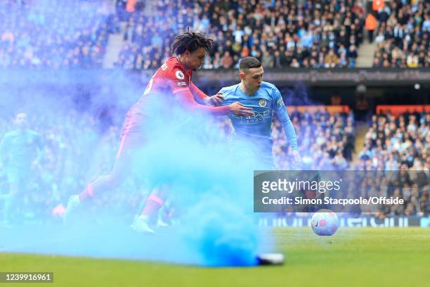 Phil Foden of Manchester City battles with Trent Alexander-Arnold of Liverpool as a blue smoke flare is set off during the Premier League match...
