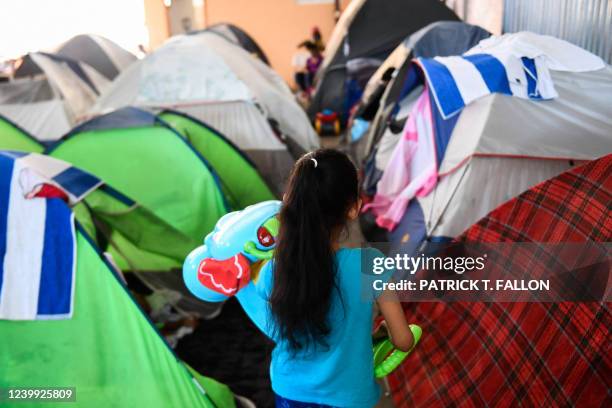 Child carries a toy as they walk past tents where they live with their family in the Movimiento Juventud 2000 shelter with refugee migrants from...
