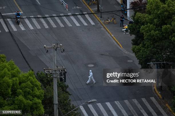 Worker wearing personal protective equipment walks on a street during a COVID-19 lockdown in the Jing'an district in Shanghai on April 12, 2022.