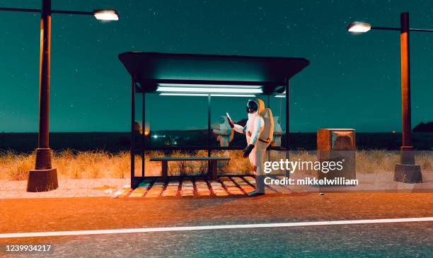 astronauta mira un teléfono móvil mientras está de pie en una parada de autobús una noche - surrealismo fotografías e imágenes de stock