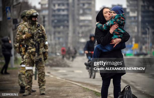 Woman holds and kisses a child next to Russian soldiers in a street of Mariupol on April 12 as Russian troops intensify a campaign to take the...