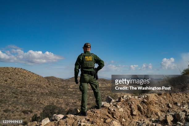 Border Patrol agent stands on a cliff looking for migrants that crossed the border wall between the U.S. And Mexico near the city of Sasabe, Arizona,...