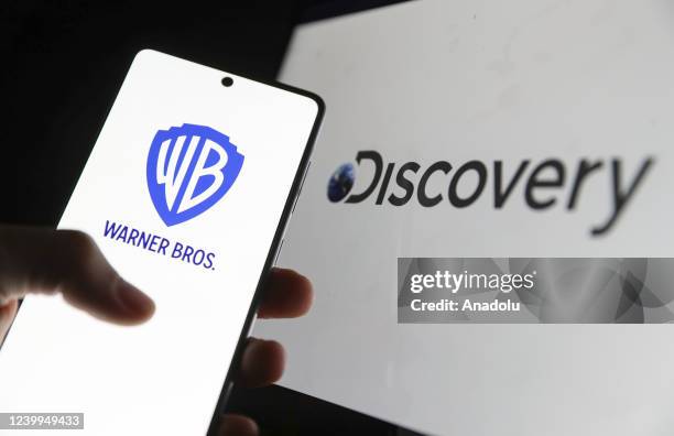 In this photo, illustration the logo of Discovery is displayed on computer screen and the logo of Warner Bros. Is displayed on phone screen in front...