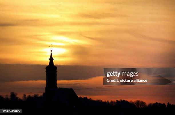 April 2022, Baden-Wuerttemberg, Munderkingen: Behind the parish church of St. Dionysius, the sun rises in the morning, also illuminating the Sahara...