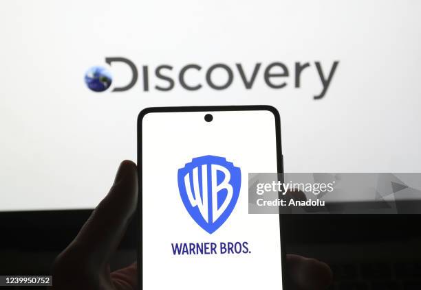 In this photo, illustration the logo of Warner Bros. Is displayed on phone screen and the logo of Discovery is displayed on computer screen back of...