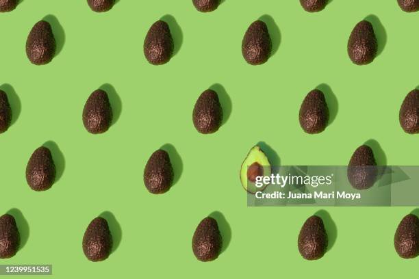 concept stand out from the crowd  large group of whole avocados placed in a repeating pattern where one split in half stands out from the crowd - vegan background stock pictures, royalty-free photos & images
