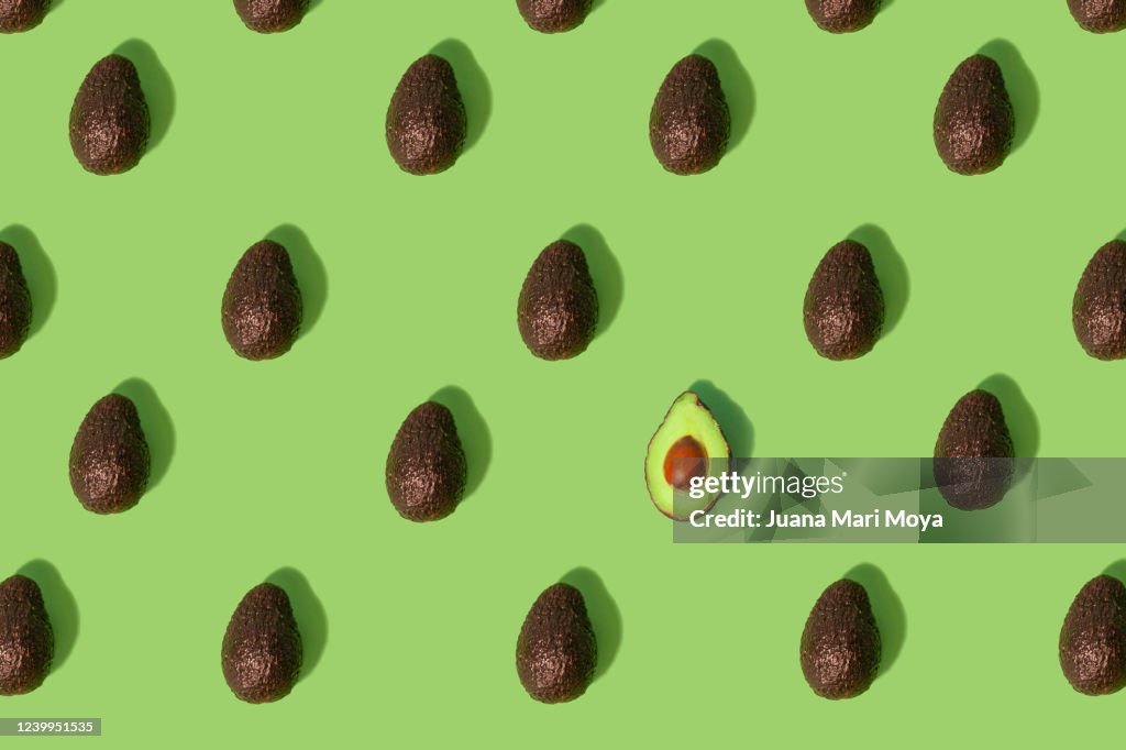 Concept stand out from the crowd  Large group of whole avocados placed in a repeating pattern where one split in half stands out from the crowd